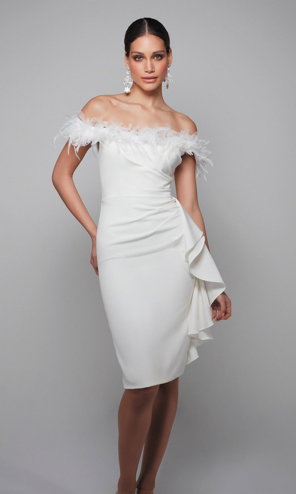 A woman poses against a plain gray background wearing the Alyce 70000 Knee Length Semi-Formal Dress in ivory, featuring an off-the-shoulder feather trim and side ruffle.